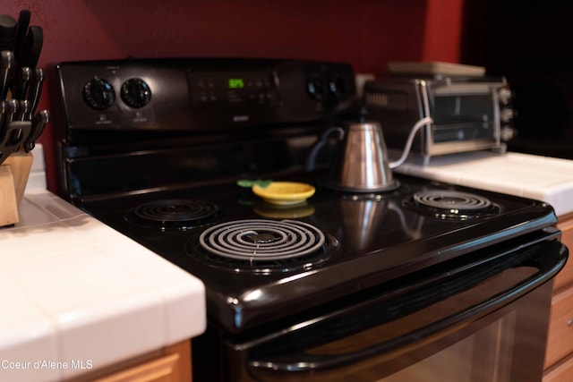 interior details with a toaster, tile countertops, and black range with electric cooktop