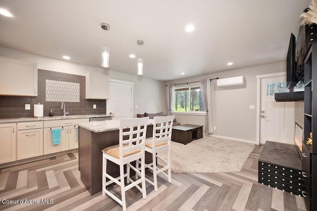 kitchen featuring a wall mounted air conditioner, a sink, a center island, decorative backsplash, and light stone countertops