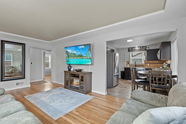 living room featuring visible vents, light wood-type flooring, baseboards, and a glass covered fireplace