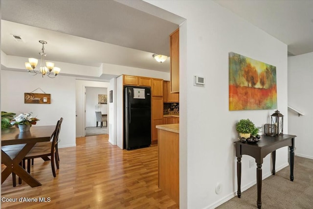 kitchen with a notable chandelier, freestanding refrigerator, light wood finished floors, light countertops, and hanging light fixtures