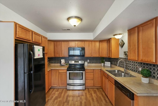 kitchen with light wood-type flooring, black appliances, a sink, light countertops, and decorative backsplash