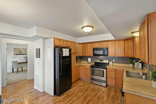 kitchen with visible vents, black appliances, light wood-style flooring, a sink, and tasteful backsplash