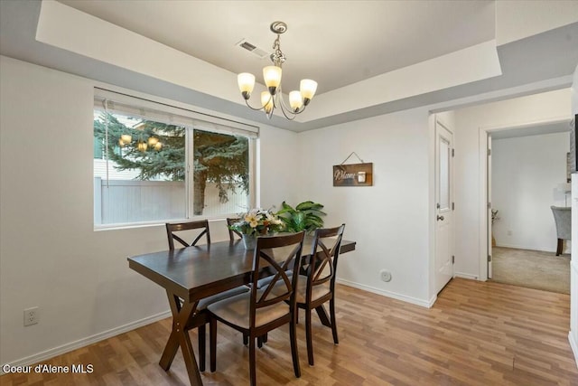 dining area with wood finished floors, baseboards, visible vents, a raised ceiling, and a chandelier