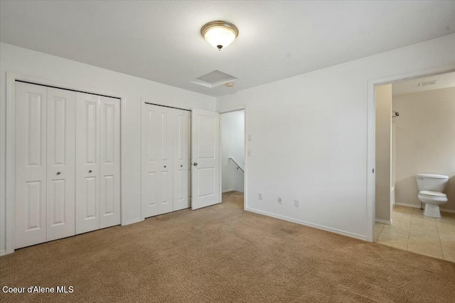 unfurnished bedroom featuring baseboards, carpet floors, two closets, and ensuite bathroom