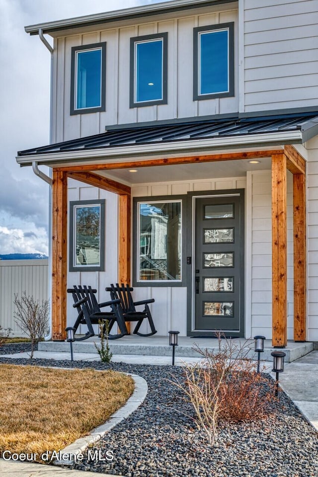 entrance to property with board and batten siding, covered porch, and fence