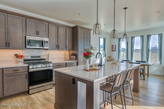 kitchen with light wood finished floors, appliances with stainless steel finishes, a breakfast bar, and light countertops