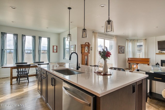 kitchen featuring a kitchen island with sink, a sink, open floor plan, light wood-style floors, and dishwasher