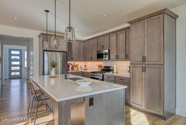 kitchen with light wood-type flooring, a kitchen island with sink, a sink, stainless steel appliances, and a breakfast bar area