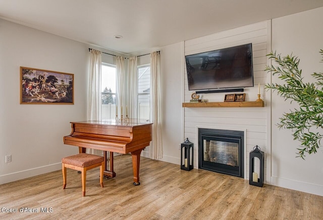 sitting room with a large fireplace, baseboards, and light wood-style flooring