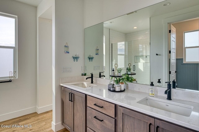 full bathroom with double vanity, a shower stall, wood finished floors, and a sink