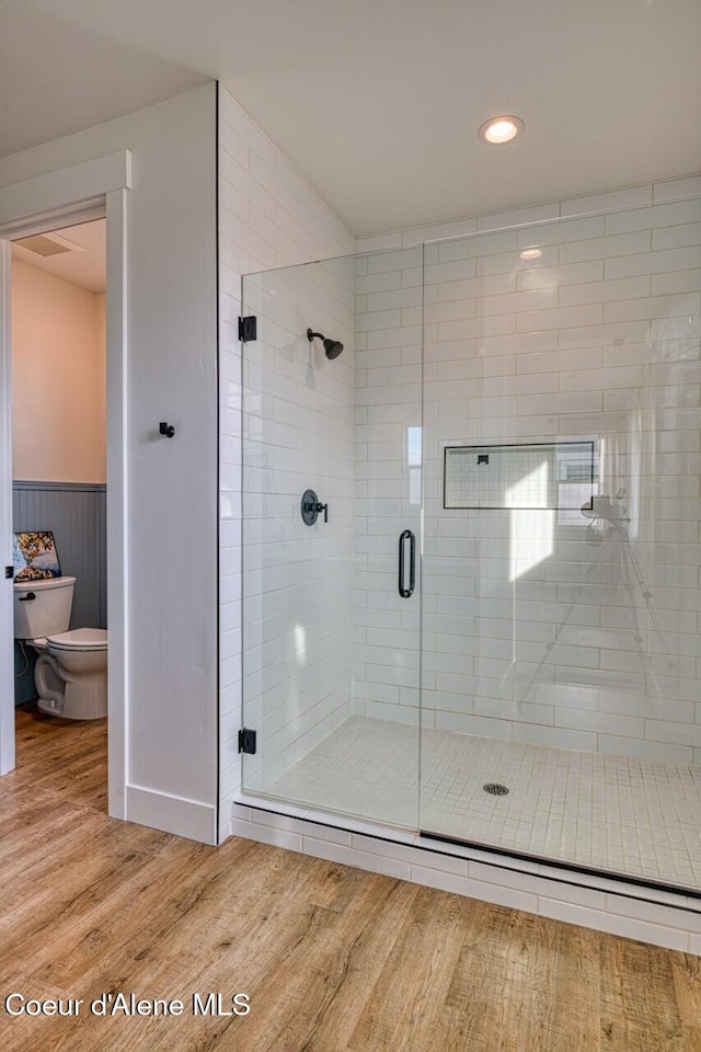 full bath featuring wainscoting, a shower stall, toilet, and wood finished floors