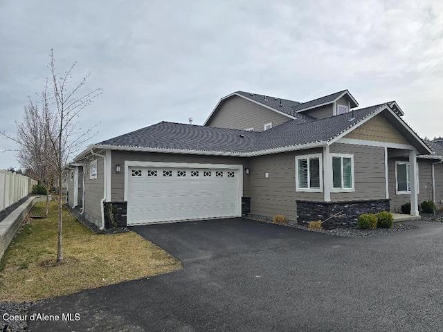 view of front of house featuring fence, an attached garage, a front lawn, stone siding, and aphalt driveway