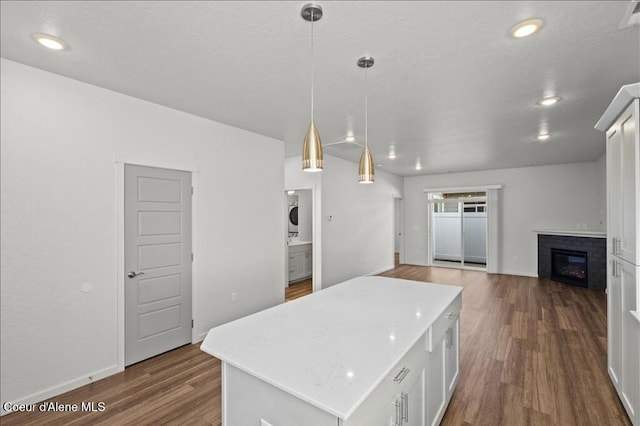 kitchen with a brick fireplace, a kitchen island, light countertops, white cabinets, and dark wood-style flooring