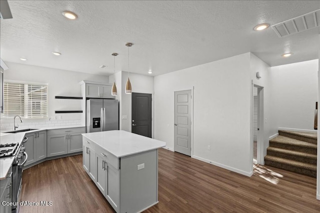 kitchen featuring visible vents, a sink, gray cabinetry, gas range oven, and stainless steel fridge