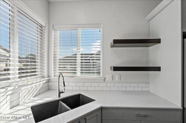 kitchen featuring open shelves, a textured wall, gray cabinets, and a sink