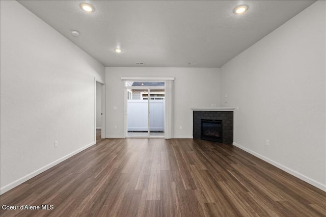 unfurnished living room featuring a brick fireplace, dark wood-style floors, and baseboards