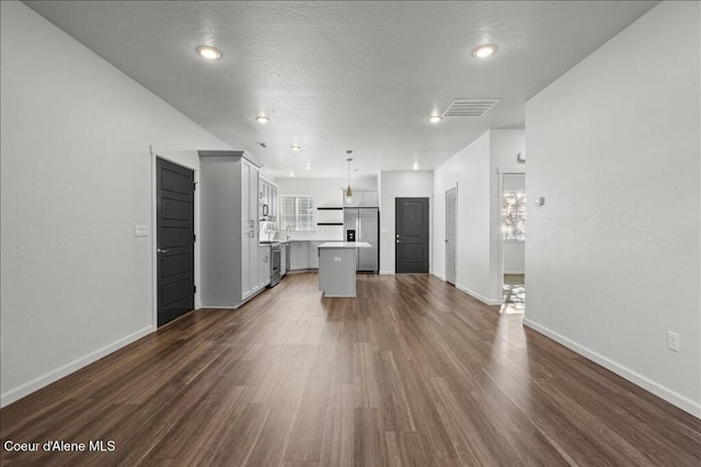 unfurnished living room featuring visible vents, baseboards, a textured ceiling, and dark wood-style flooring