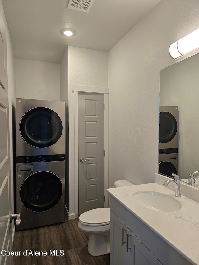 bathroom featuring visible vents, toilet, stacked washer and clothes dryer, wood finished floors, and vanity