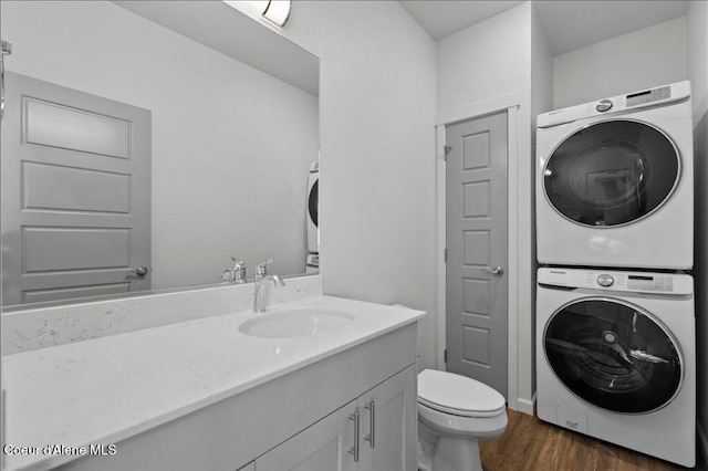 bathroom featuring stacked washer / dryer, toilet, vanity, and wood finished floors