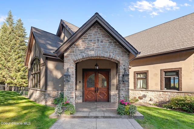 doorway to property with stucco siding, stone siding, a lawn, and a shingled roof