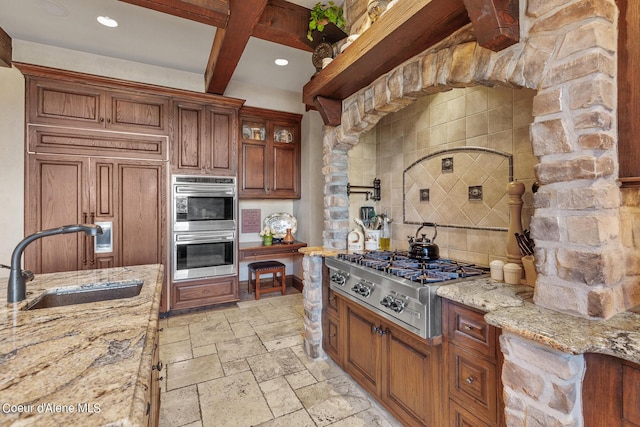 kitchen featuring a sink, light stone counters, stone tile floors, appliances with stainless steel finishes, and decorative backsplash