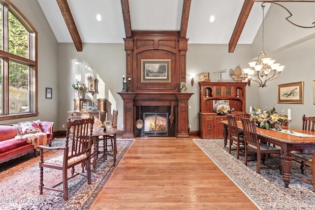 dining area with lofted ceiling with beams, a notable chandelier, a fireplace, and light wood finished floors