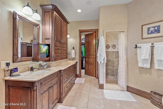 bathroom featuring vanity, baseboards, tiled shower, tile patterned flooring, and a closet