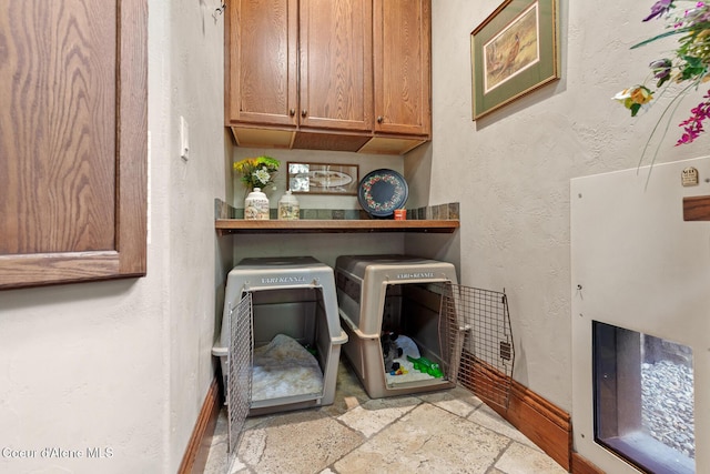 laundry room featuring baseboards, a textured wall, stone tile flooring, cabinet space, and separate washer and dryer