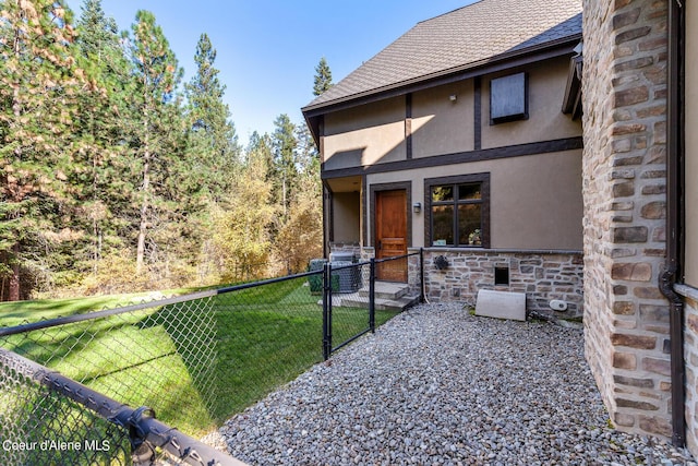 back of property featuring stone siding, stucco siding, a lawn, and roof with shingles