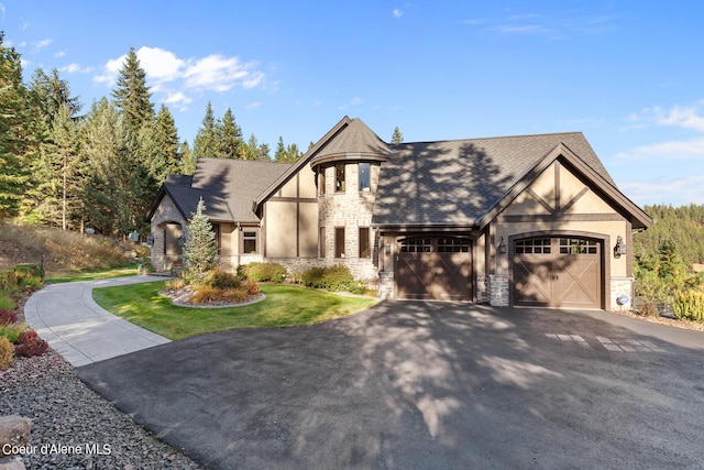 tudor home with an attached garage, stone siding, driveway, and stucco siding