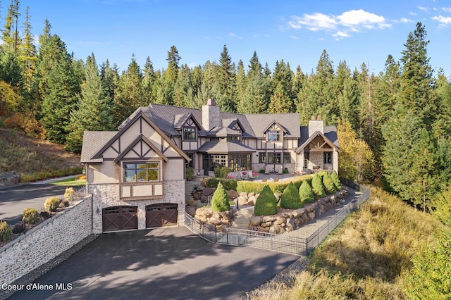 view of front of property featuring stucco siding, aphalt driveway, stone siding, a forest view, and an attached garage