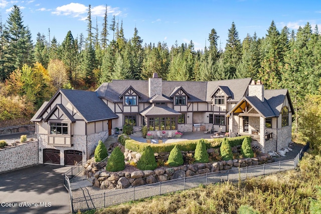 tudor house with stucco siding, stone siding, fence, an attached garage, and a patio area