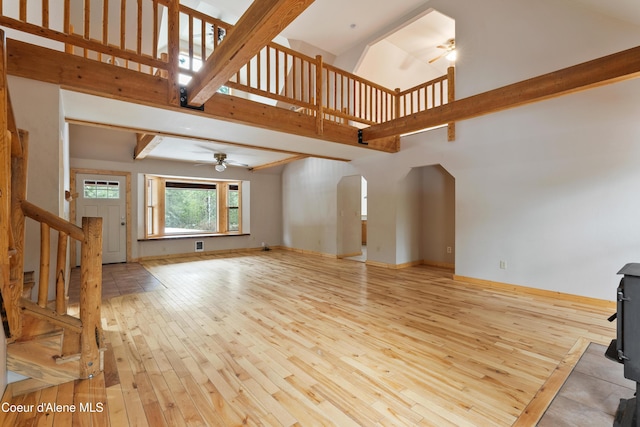 unfurnished living room with ceiling fan, stairway, light wood-type flooring, a high ceiling, and arched walkways