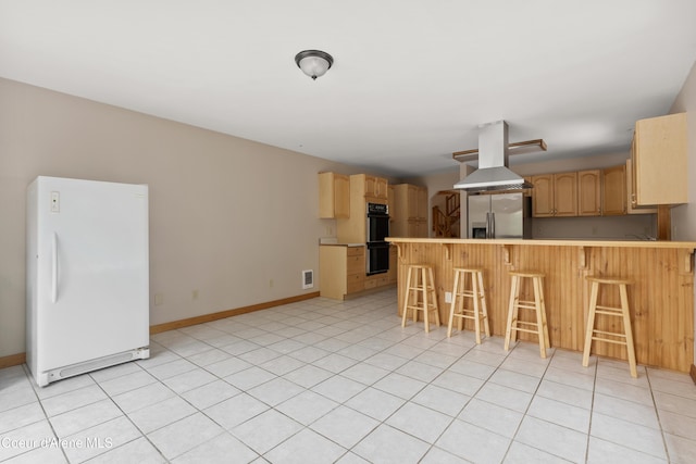 kitchen featuring a peninsula, island exhaust hood, freestanding refrigerator, dobule oven black, and stainless steel fridge