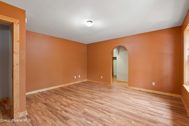 spare room featuring arched walkways, baseboards, and light wood-style floors