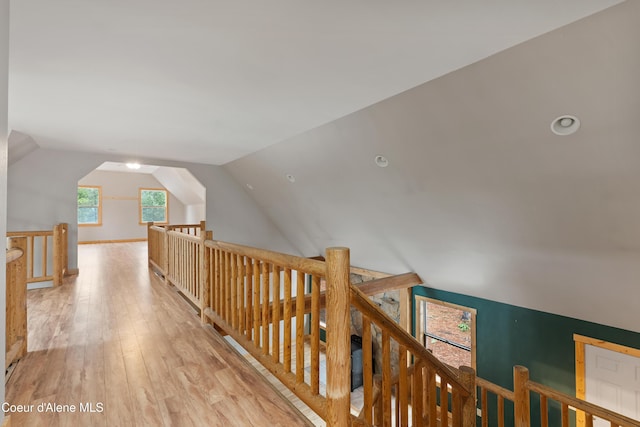 hall with an upstairs landing, light wood-type flooring, and lofted ceiling