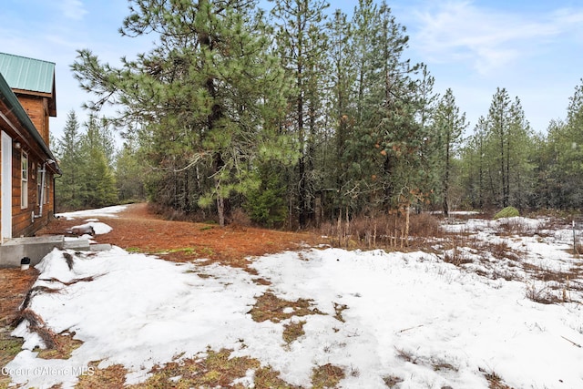 yard covered in snow featuring a wooded view