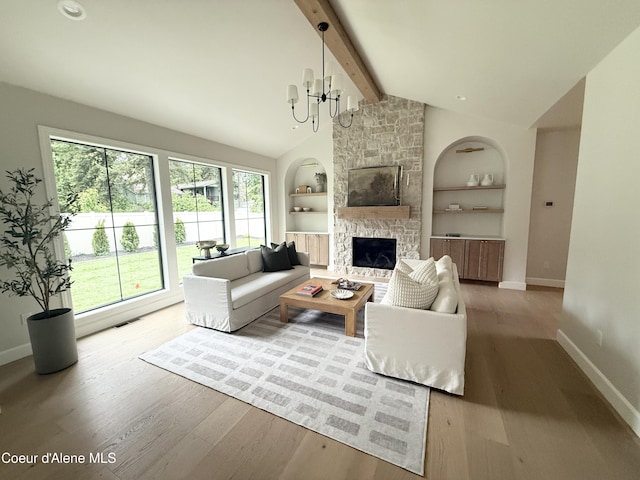 living area featuring baseboards, built in features, wood finished floors, a stone fireplace, and a chandelier