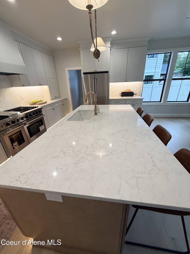 kitchen featuring premium appliances, a sink, a kitchen bar, light stone counters, and recessed lighting
