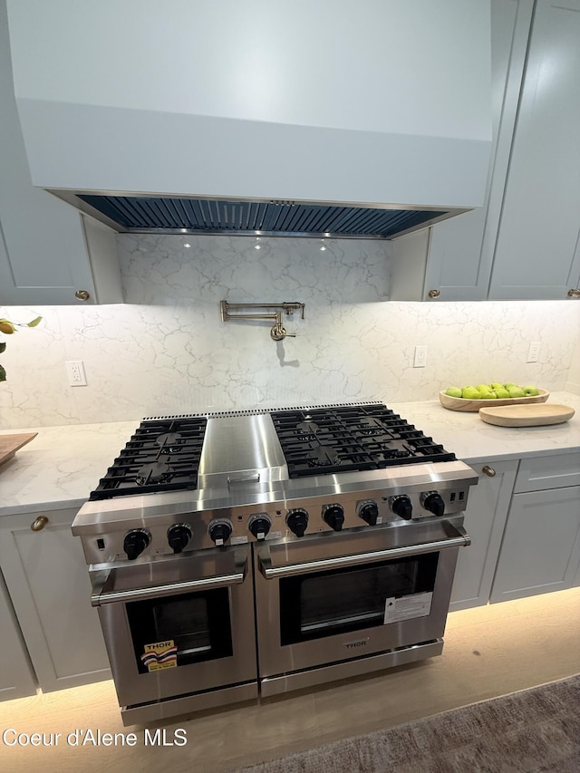 kitchen featuring custom range hood, double oven range, backsplash, and light stone countertops