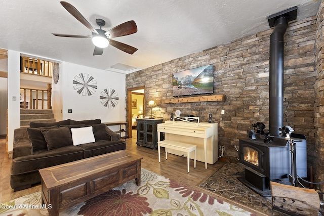 living room with a ceiling fan, wood finished floors, a wood stove, and a textured ceiling