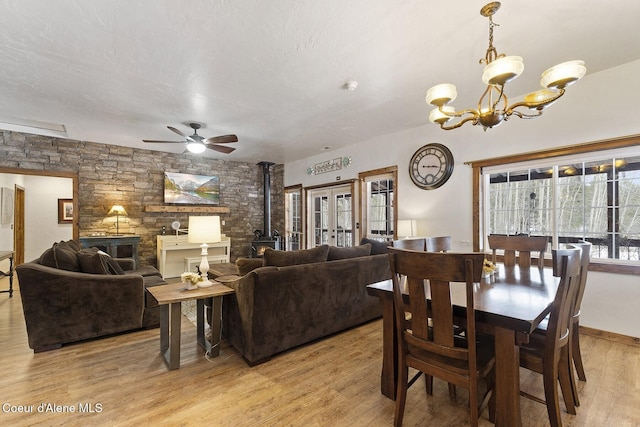 dining space with light wood finished floors, ceiling fan with notable chandelier, a textured ceiling, and a wood stove