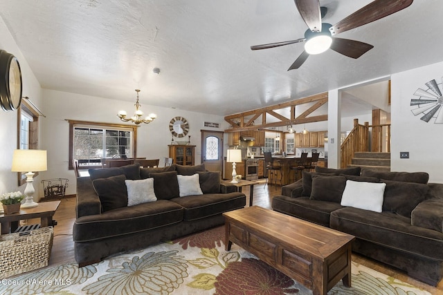 living room with a textured ceiling, wood finished floors, stairs, and ceiling fan with notable chandelier