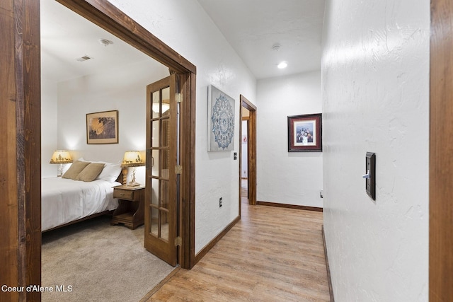 hallway with visible vents, a textured wall, baseboards, and light wood finished floors