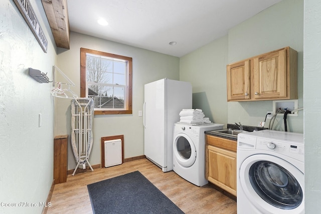 laundry area with washing machine and dryer, cabinet space, light wood finished floors, and a sink