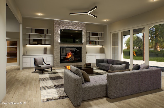 living room with built in features, light wood-style flooring, a large fireplace, and a ceiling fan