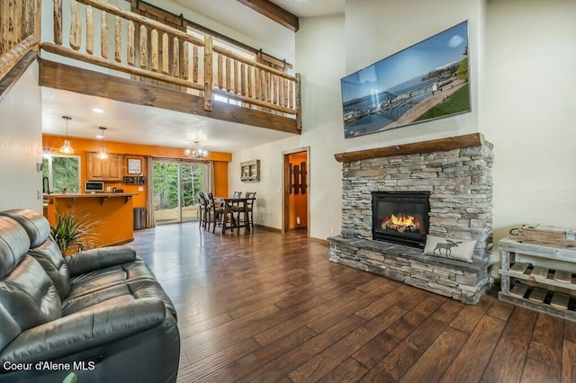 living area with a stone fireplace, an inviting chandelier, a towering ceiling, and wood-type flooring
