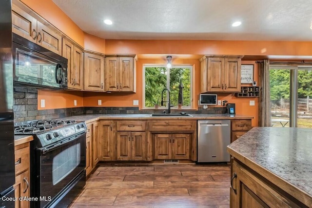 kitchen with a sink, black appliances, dark wood-type flooring, and plenty of natural light