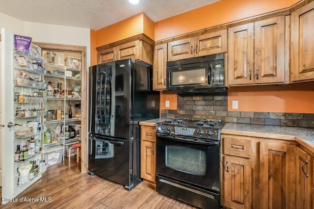 kitchen featuring black appliances, light wood-style flooring, light countertops, and backsplash