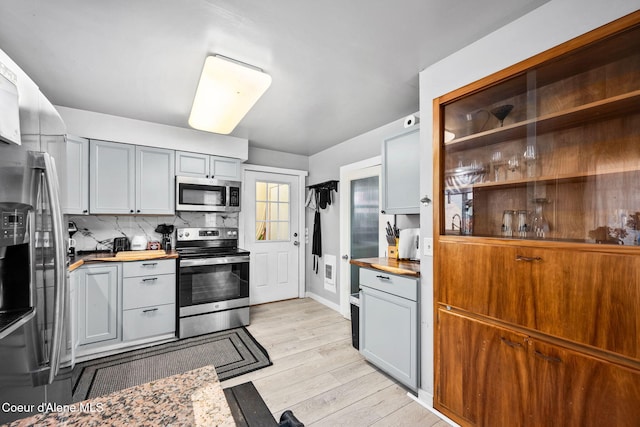 kitchen with gray cabinetry, decorative backsplash, butcher block countertops, stainless steel appliances, and light wood-type flooring
